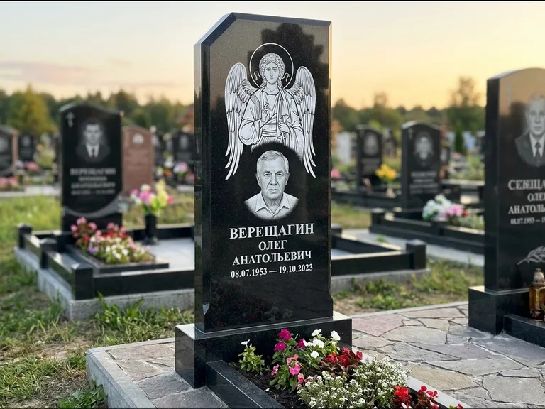 Памятник с гравировкой иконы: стела с резным навершием и нимбом в золоте — гравировка образа Спасителя, высокие разросшиеся туи полукругом, работа «Мельникова» в Липецке