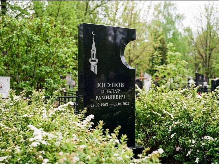 Мусульманский памятник с гравировкой мечети: стела с боковым вырезом в форме полумесяца — гравировка минарета с полумесяцем, низкие кусты спиреи в цвету, работа «Юсупов» в Липецке